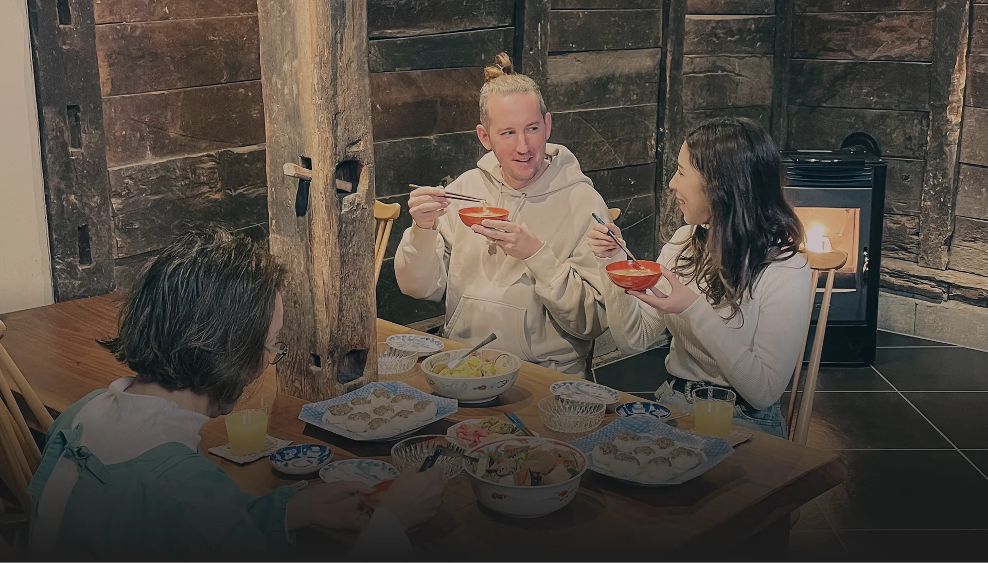 囲炉裏のある伝統的な雰囲気の部屋で、数人の人々がテーブルを囲んで楽しそうに食事をしている様子。