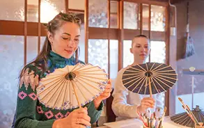 明るい室内で、2人の女性が伝統的な和傘（唐傘）を手に持って広げ、嬉しそうに眺めている様子。