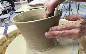 ろくろの上で回転する粘土に両手を添え、器の形へと丁寧に成形している陶芸の様子。