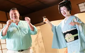 着物姿の芸者と笑顔の外国人男性が、お座敷で楽しそうにお座敷遊びやお酒を酌み交わしている様子。