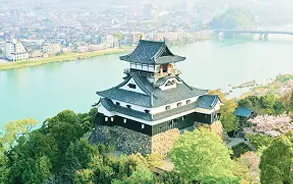 川のほとりに佇む、緑豊かな山の上に建てられた歴史的な日本の城（天守閣）の全景。